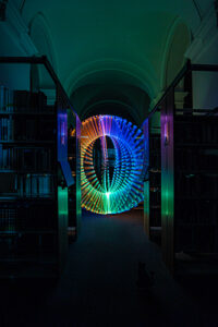 bunter Lightpainting Orb zwischen Bücherregalen der Bibliotheca Albertina im Vordergrund sitzt eine Katze