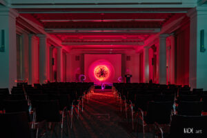 Zu sehen ist ein pinker Orb mit orangenem Zentrum. Er wurde auf der Bühne im Vortragsraum der BIbliotheca Albertina mit licht gemalt