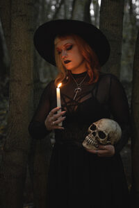 Hexe im schwarzen Kleid mit Pentagram auf der Brust hält in der einen Hand einen Schädel und in der anderen eine Kerze Die stimmung ist sehr düster