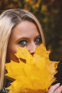 Portraitshooing im Herbst mit Veronika. Gesicht versteckt hinter einem großen gelben Ahornblatt
