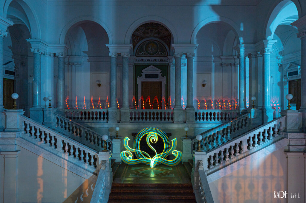 Lightpainting in der Bibliotheca Albertina Auf der oberen Galerie wurde wieder ein Spiraltunnel in Rot gezogen. Auf der mittleren Ebene, vor der Schneiderbank habe ich ein florales Element gesteztz. Es hat die Farben gelb und blau und wirkt dadurch grün