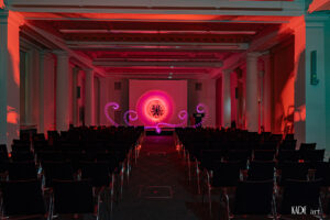 Zu sehen ist ein pinker Orb mit orangenem Zentrum. Er wurde auf der Bühne im Vortragsraum der BIbliotheca Albertina mit licht gemalt